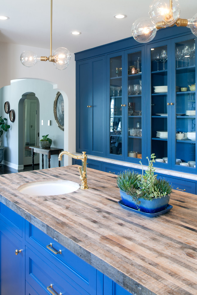 Photo of a large mediterranean u-shaped eat-in kitchen in Los Angeles with a farmhouse sink, recessed-panel cabinets, blue cabinets, marble benchtops, white splashback, ceramic splashback, panelled appliances, concrete floors and with island.