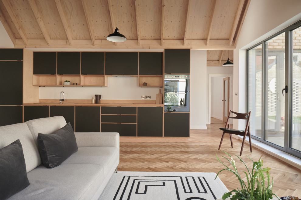 Inspiration for a large contemporary open plan kitchen in London with flat-panel cabinets, green cabinets, wood worktops, light hardwood flooring, a breakfast bar and a vaulted ceiling.