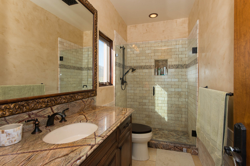 Mid-sized mediterranean master bathroom in Los Angeles with raised-panel cabinets, dark wood cabinets, a drop-in tub, a corner shower, beige tile, black tile, brown tile, gray tile, stone slab, beige walls, travertine floors, an undermount sink and marble benchtops.