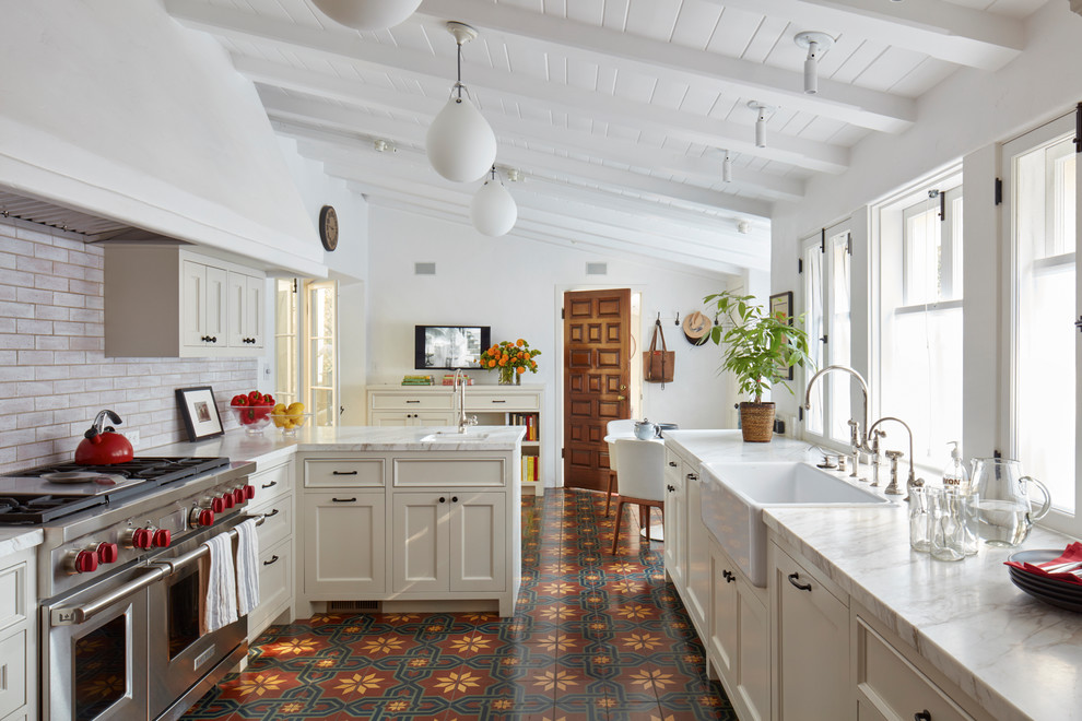 This is an example of a mediterranean eat-in kitchen in Los Angeles with a farmhouse sink, marble benchtops, cement tiles, a peninsula, multi-coloured floor, beige cabinets, subway tile splashback, stainless steel appliances, recessed-panel cabinets and beige benchtop.