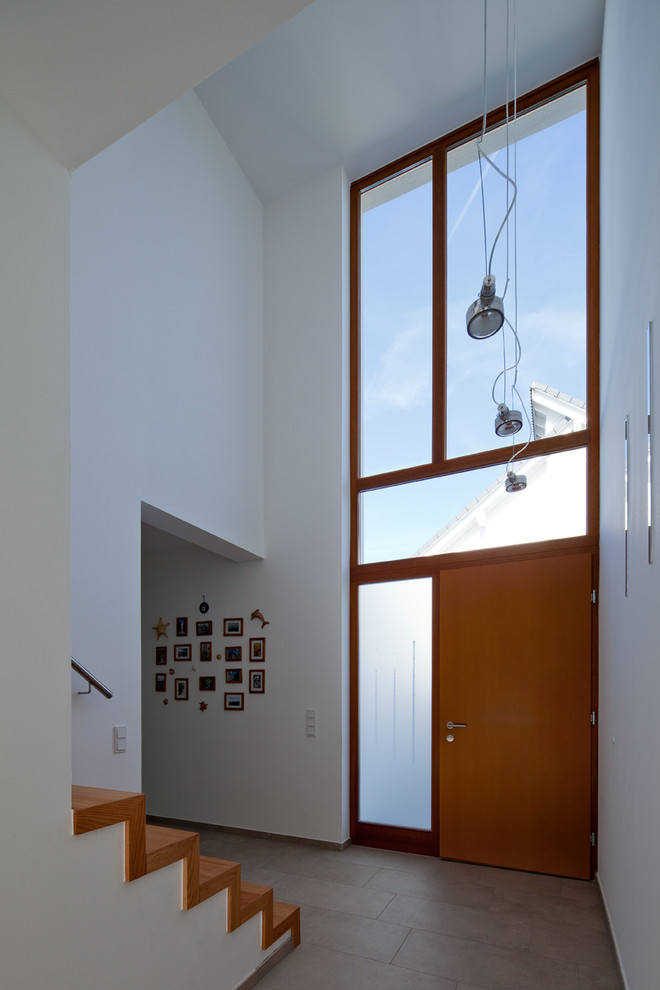 Geräumiger Moderner Eingang mit Vestibül, weißer Wandfarbe, Keramikboden, Einzeltür und hellbrauner Holzhaustür in Köln