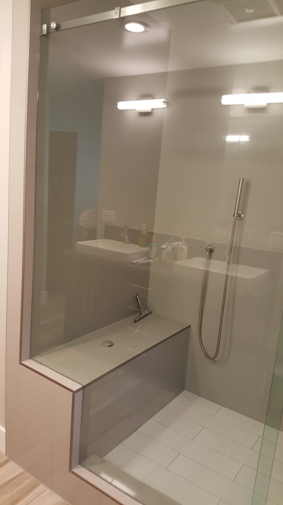 This is an example of a large modern master bathroom in Los Angeles with shaker cabinets, black cabinets, an alcove shower, a one-piece toilet, gray tile, ceramic tile, grey walls, wood-look tile, a drop-in sink, solid surface benchtops, brown floor, a hinged shower door, black benchtops, a shower seat, a double vanity and a built-in vanity.