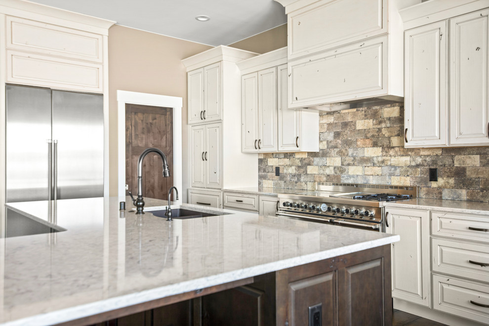 Eat-in kitchen - large transitional l-shaped medium tone wood floor and brown floor eat-in kitchen idea with an undermount sink, raised-panel cabinets, quartz countertops, beige backsplash, stone tile backsplash, stainless steel appliances, an island and beige countertops