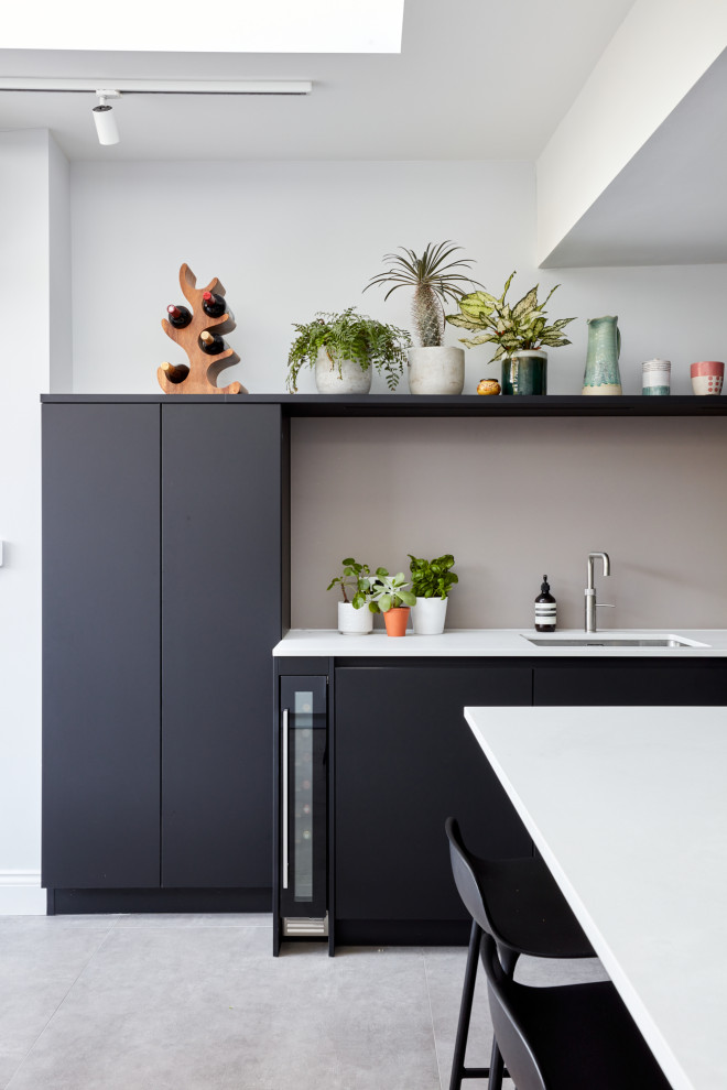 Example of a mid-sized minimalist u-shaped eat-in kitchen design in London with an integrated sink, flat-panel cabinets, black cabinets, quartz countertops, pink backsplash, glass sheet backsplash, stainless steel appliances, an island and white countertops