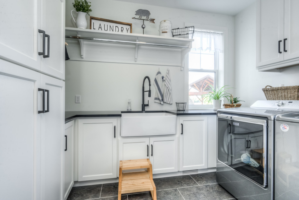 Photo of a mid-sized country u-shaped dedicated laundry room in Toronto with a farmhouse sink, shaker cabinets, white cabinets, granite benchtops, white walls, ceramic floors, a side-by-side washer and dryer, black floor and black benchtop.