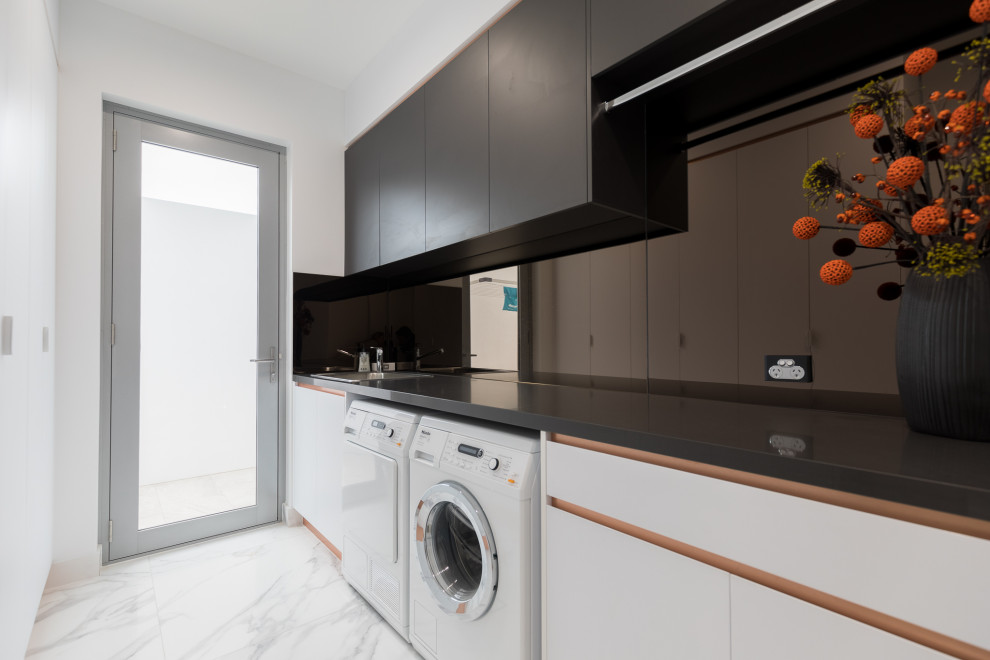 Contemporary galley dedicated laundry room in Gold Coast - Tweed with a side-by-side washer and dryer and black benchtop.