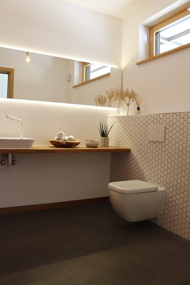 Photo of a modern powder room in Other with a wall-mount toilet, white walls, a vessel sink, wood benchtops, black floor and brown benchtops.
