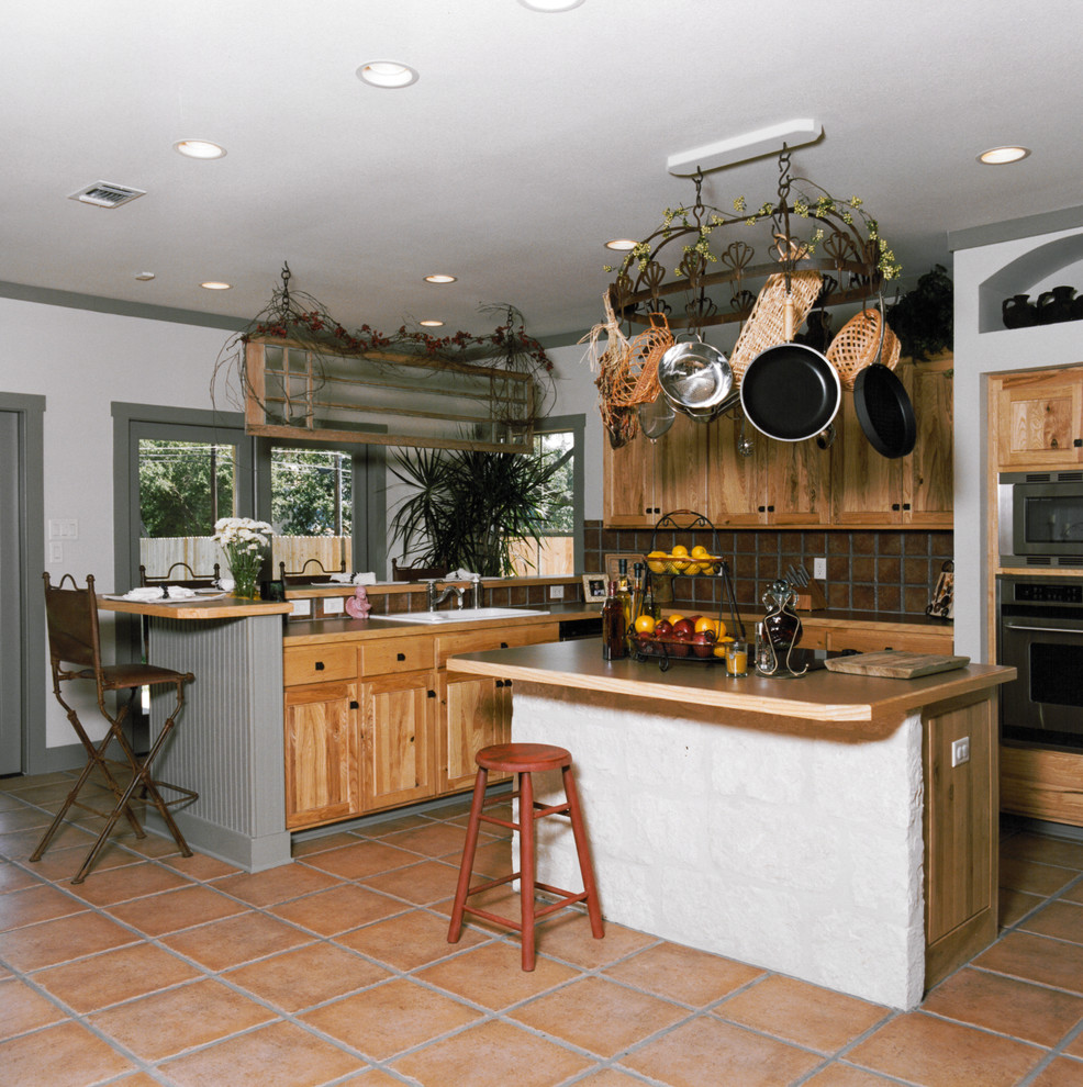 Example of a mountain style terra-cotta tile eat-in kitchen design in Austin with medium tone wood cabinets, wood countertops, red backsplash, terra-cotta backsplash, stainless steel appliances and an island