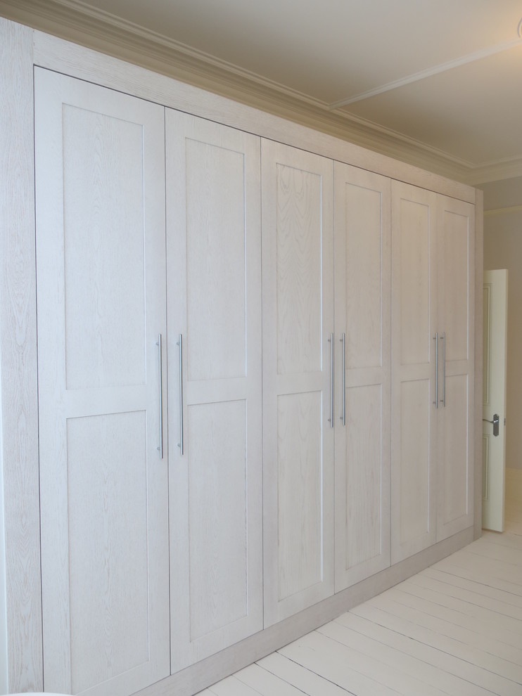 Large contemporary gender-neutral dressing room in London with shaker cabinets, light wood cabinets, painted wood floors and white floor.