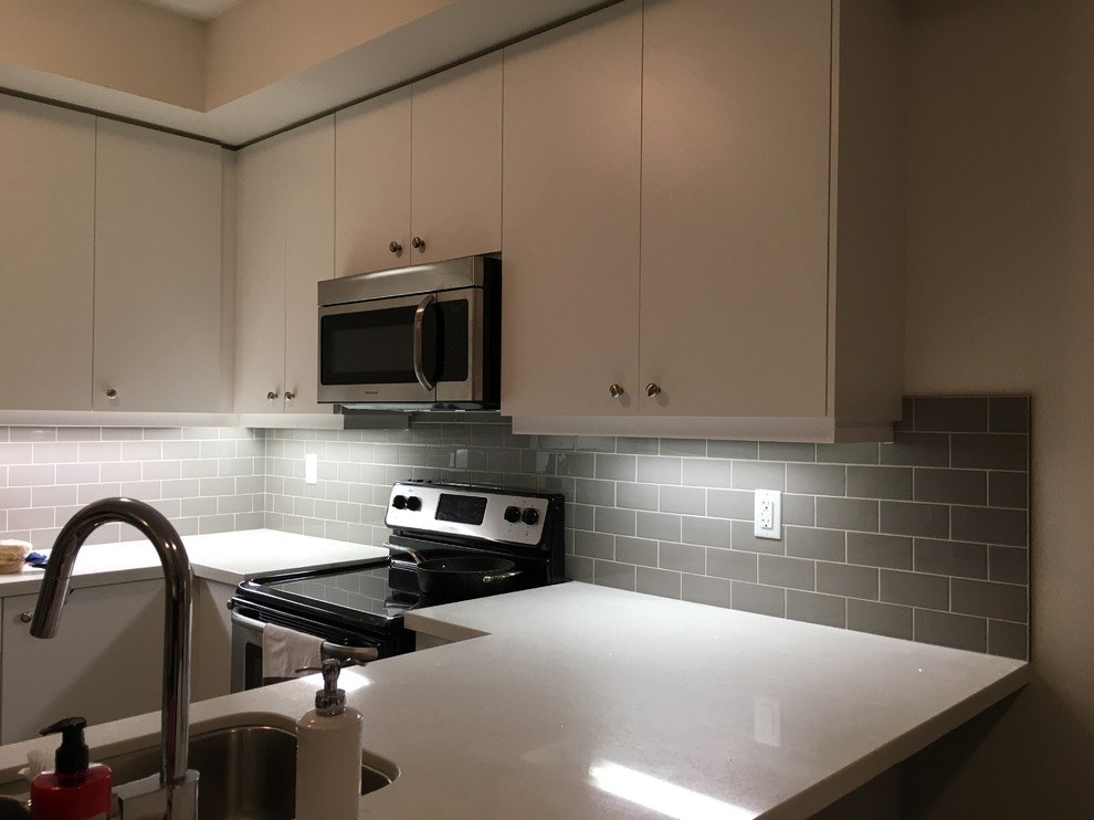 Photo of a mid-sized transitional l-shaped eat-in kitchen in Toronto with an undermount sink, flat-panel cabinets, white cabinets, quartz benchtops, grey splashback, subway tile splashback, stainless steel appliances and white benchtop.