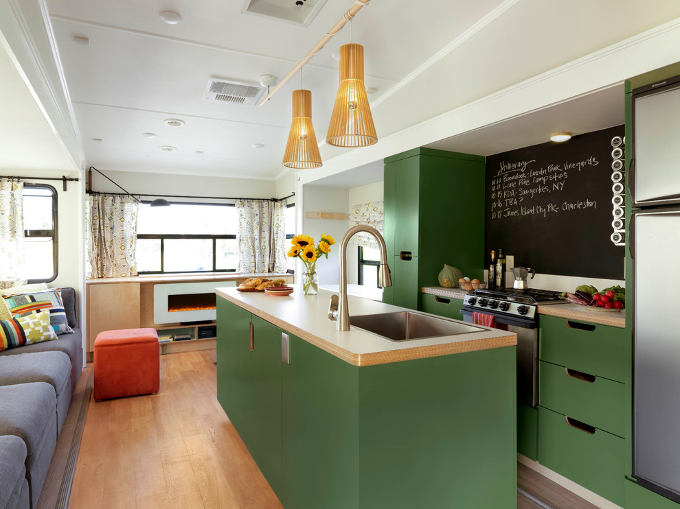 This is an example of a small eclectic galley eat-in kitchen in Burlington with a single-bowl sink, flat-panel cabinets, green cabinets, laminate benchtops, black splashback, stainless steel appliances, light hardwood floors and with island.