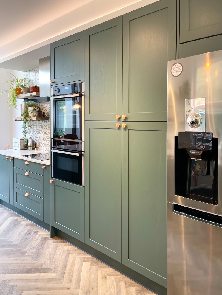 Immagine di una cucina minimalista di medie dimensioni con lavello sottopiano, ante in stile shaker, ante verdi, top in marmo, elettrodomestici neri, parquet chiaro, pavimento marrone e top bianco