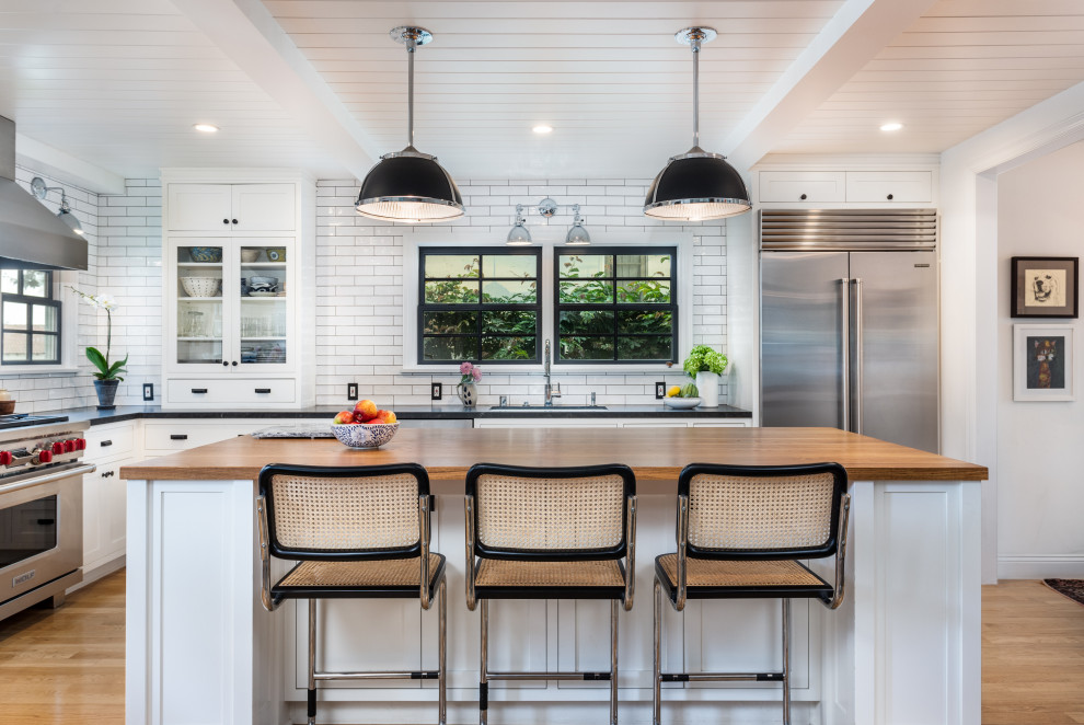 Inspiration for a mid-sized country l-shaped eat-in kitchen in Los Angeles with an undermount sink, shaker cabinets, white cabinets, wood benchtops, white splashback, subway tile splashback, stainless steel appliances, light hardwood floors, with island, brown benchtop, timber and beige floor.