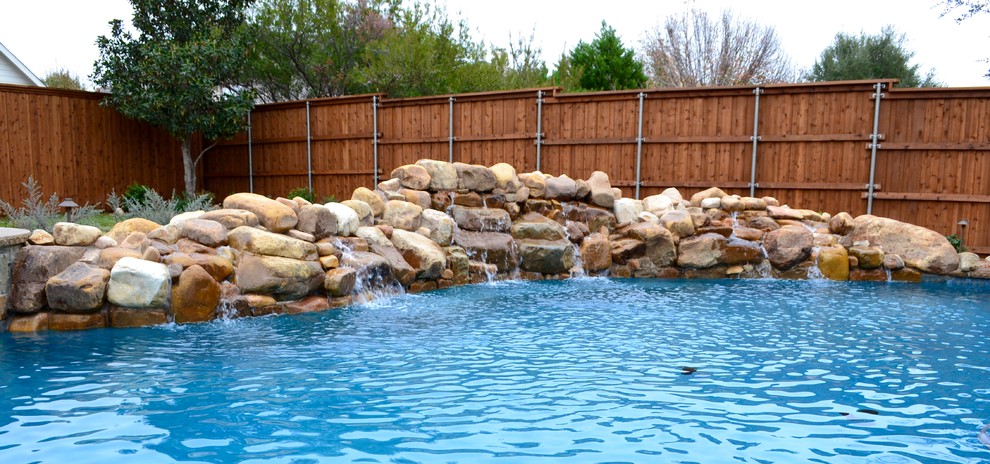 This is an example of a mid-sized contemporary backyard custom-shaped natural pool in Dallas with a water feature and natural stone pavers.