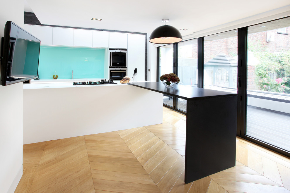 Mid-sized contemporary l-shaped open plan kitchen in Manchester with a drop-in sink, flat-panel cabinets, white cabinets, light hardwood floors and with island.