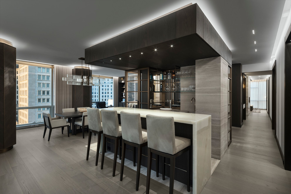 Photo of a contemporary seated home bar in New York with mirror splashback, light hardwood floors and white benchtop.