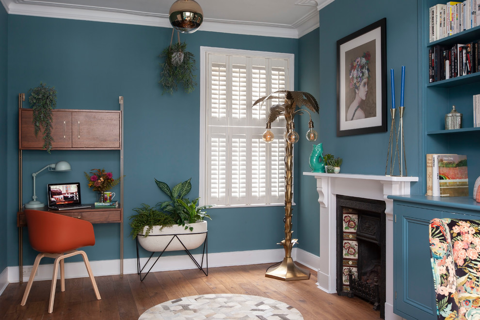 Inspiration for a mid-sized eclectic study room in London with blue walls, brown floor, dark hardwood floors, a standard fireplace and a freestanding desk.