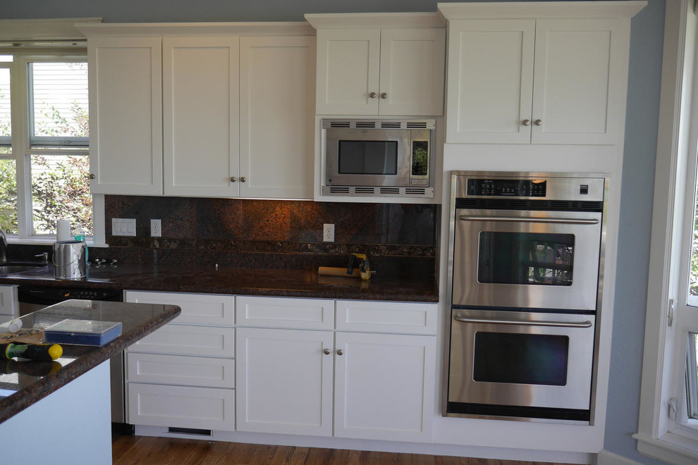 Example of a mid-sized transitional medium tone wood floor eat-in kitchen design in Denver with shaker cabinets, white cabinets, granite countertops, stainless steel appliances and a peninsula