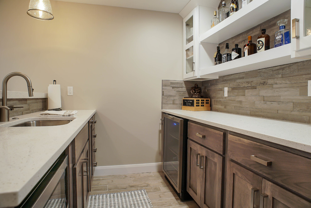 This is an example of a mid-sized contemporary galley home bar in Salt Lake City with an undermount sink, solid surface benchtops, beige splashback, porcelain splashback, light hardwood floors, beige floor, shaker cabinets and medium wood cabinets.