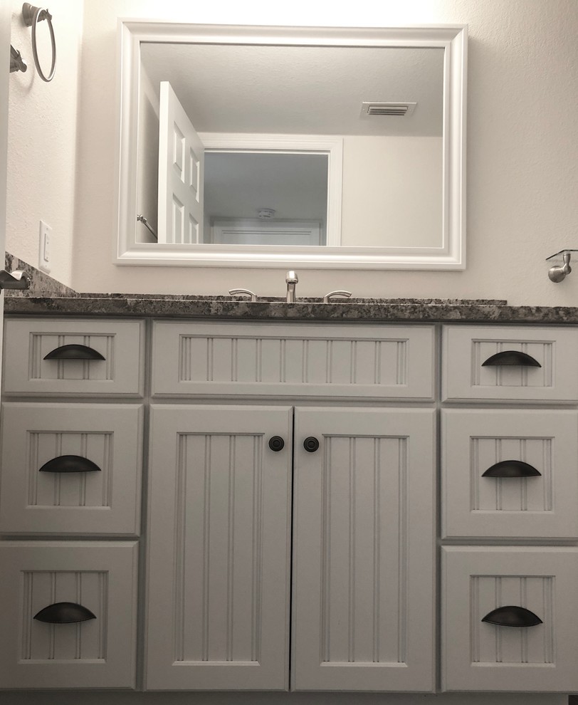 Photo of a mid-sized transitional 3/4 bathroom in Tampa with recessed-panel cabinets, white cabinets, an alcove tub, a shower/bathtub combo, a two-piece toilet, gray tile, porcelain tile, beige walls, dark hardwood floors, an undermount sink, granite benchtops, brown floor, a sliding shower screen and beige benchtops.