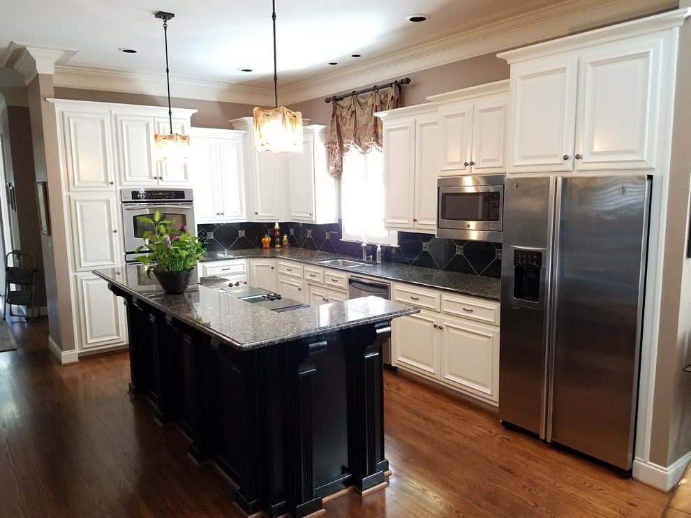 Photo of a mid-sized transitional l-shaped eat-in kitchen in Birmingham with a double-bowl sink, raised-panel cabinets, white cabinets, quartz benchtops, black splashback, porcelain splashback, stainless steel appliances, medium hardwood floors and with island.