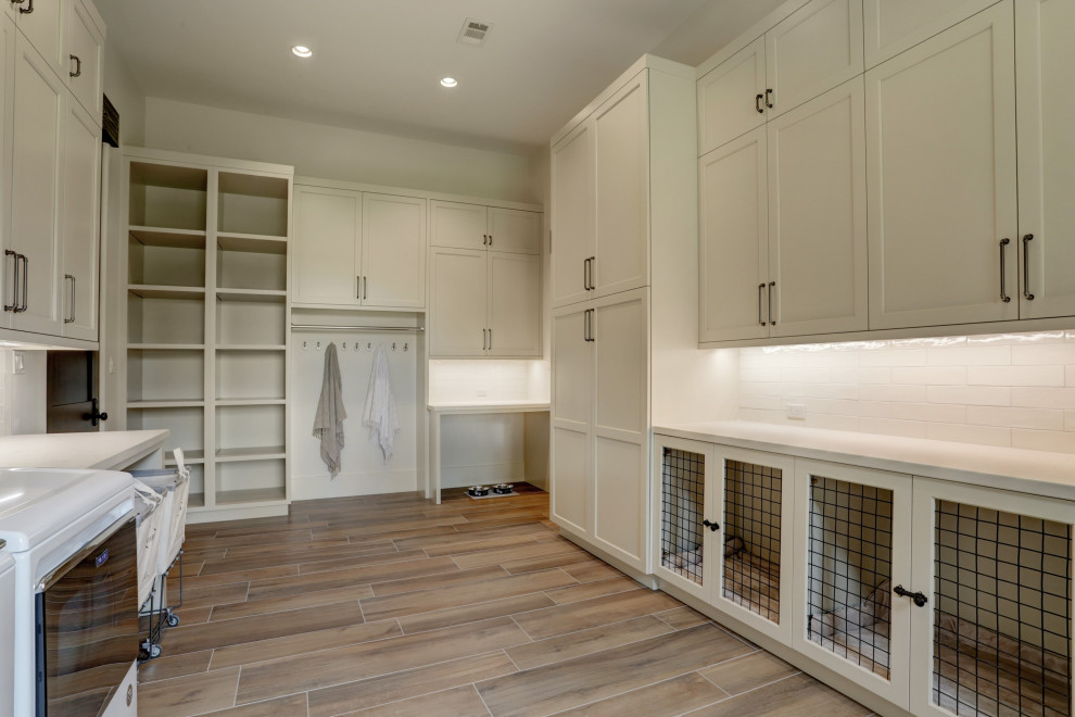This is an example of a country laundry room in Houston with shaker cabinets, distressed cabinets, quartz benchtops, beige splashback, subway tile splashback, beige walls, porcelain floors, a side-by-side washer and dryer, brown floor and beige benchtop.