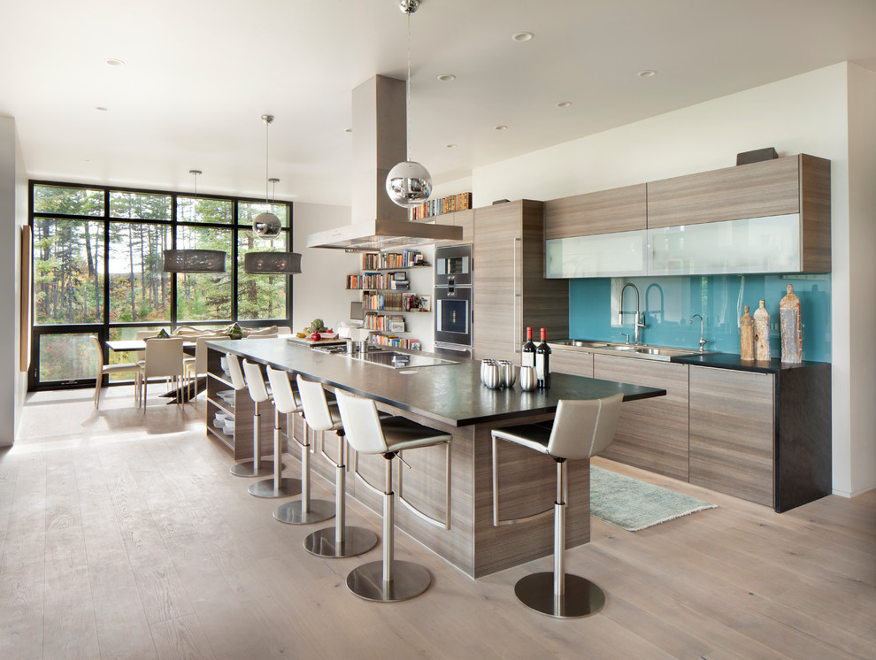Contemporary galley kitchen in Other with flat-panel cabinets, grey cabinets, blue splashback, glass sheet splashback, medium hardwood floors, with island and brown floor.
