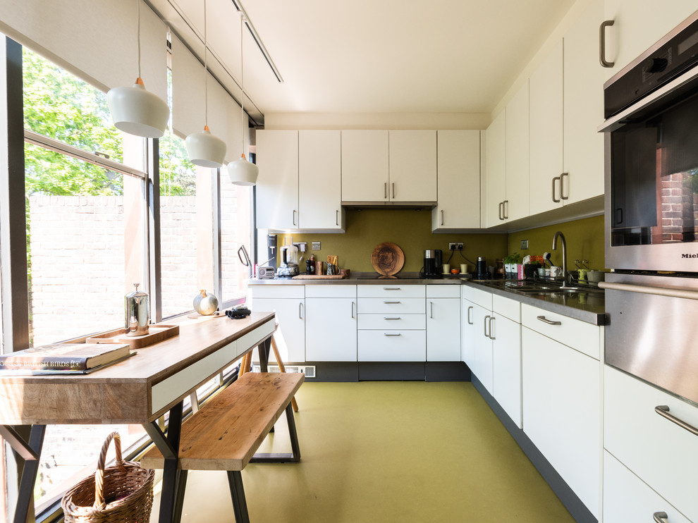 Mid-sized midcentury l-shaped eat-in kitchen in London with flat-panel cabinets, white cabinets, granite benchtops, green splashback, stainless steel appliances, no island, green floor, black benchtop and a double-bowl sink.