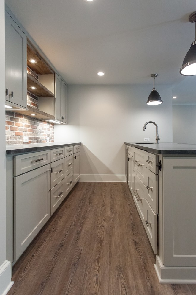 Photo of a traditional galley wet bar in DC Metro with brown floor, an undermount sink, shaker cabinets, grey cabinets, multi-coloured splashback, brick splashback and black benchtop.