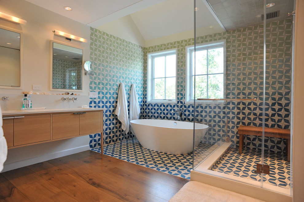 Photo of a large contemporary master bathroom in New York with flat-panel cabinets, medium wood cabinets, a freestanding tub, a corner shower, a one-piece toilet, blue tile, green tile, multi-coloured tile, cement tile, white walls, medium hardwood floors, an undermount sink, engineered quartz benchtops, brown floor and a hinged shower door.
