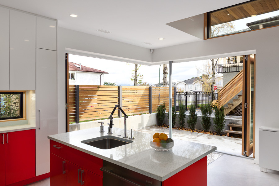 Inspiration for a modern l-shaped open plan kitchen in Vancouver with an undermount sink, flat-panel cabinets, red cabinets, quartz benchtops, blue splashback, glass sheet splashback, stainless steel appliances, concrete floors and with island.
