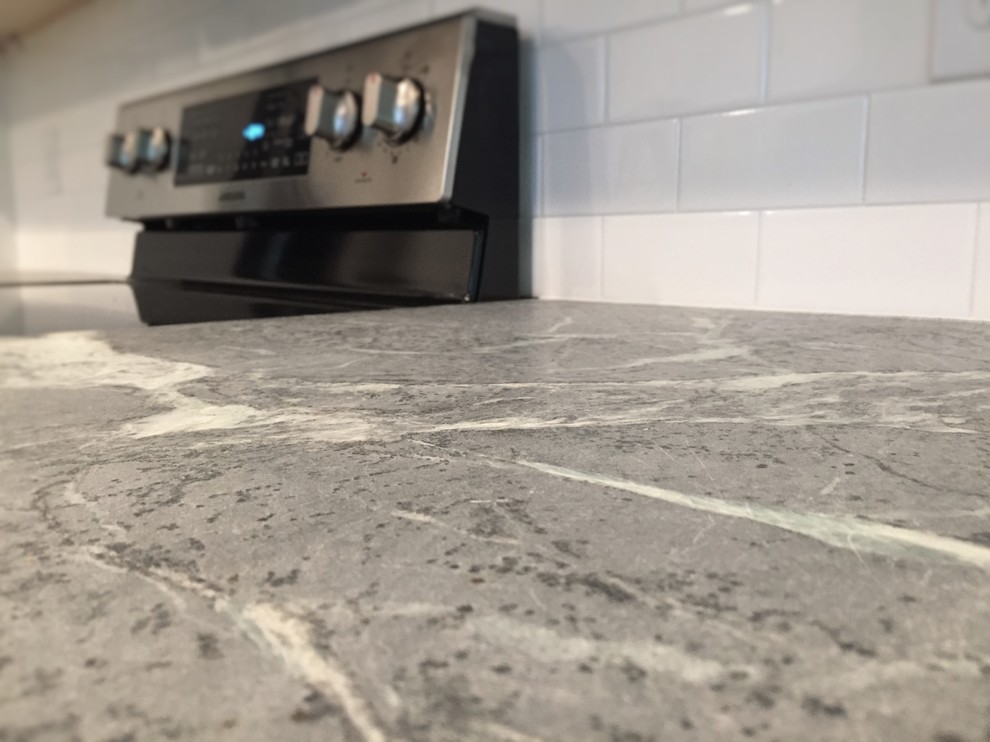 Inspiration for a mid-sized transitional l-shaped medium tone wood floor enclosed kitchen remodel with an undermount sink, shaker cabinets, white cabinets, soapstone countertops, white backsplash, subway tile backsplash, stainless steel appliances and a peninsula