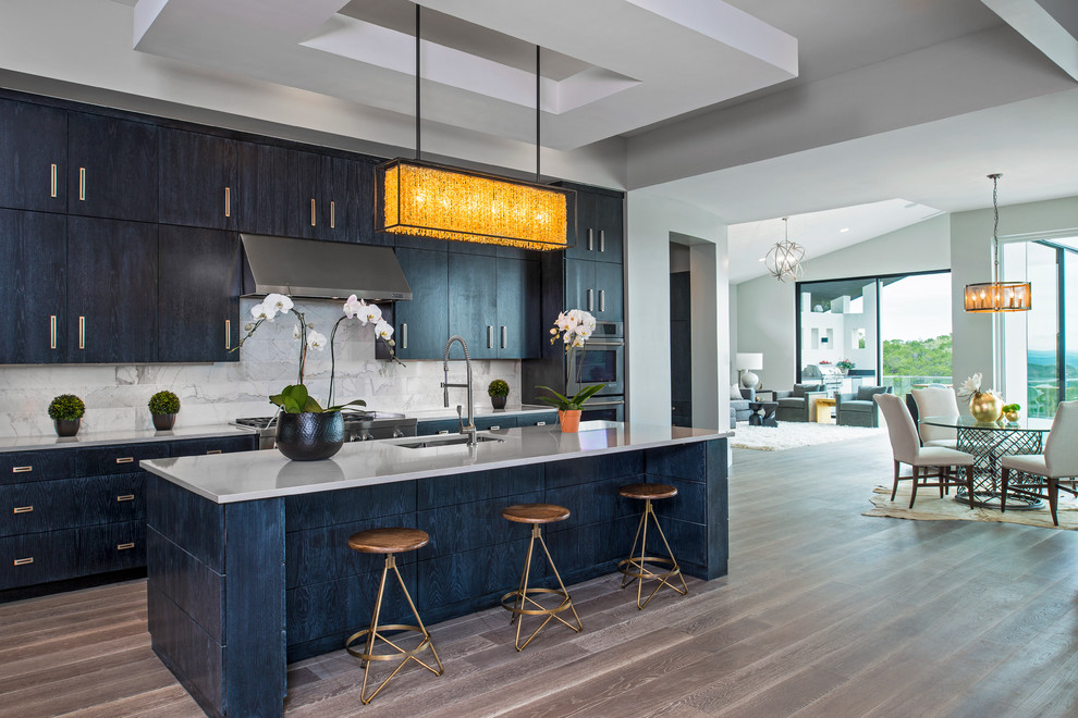 This is an example of an expansive contemporary galley open plan kitchen in Austin with an undermount sink, flat-panel cabinets, dark wood cabinets, quartz benchtops, grey splashback, stone tile splashback, stainless steel appliances, light hardwood floors and with island.