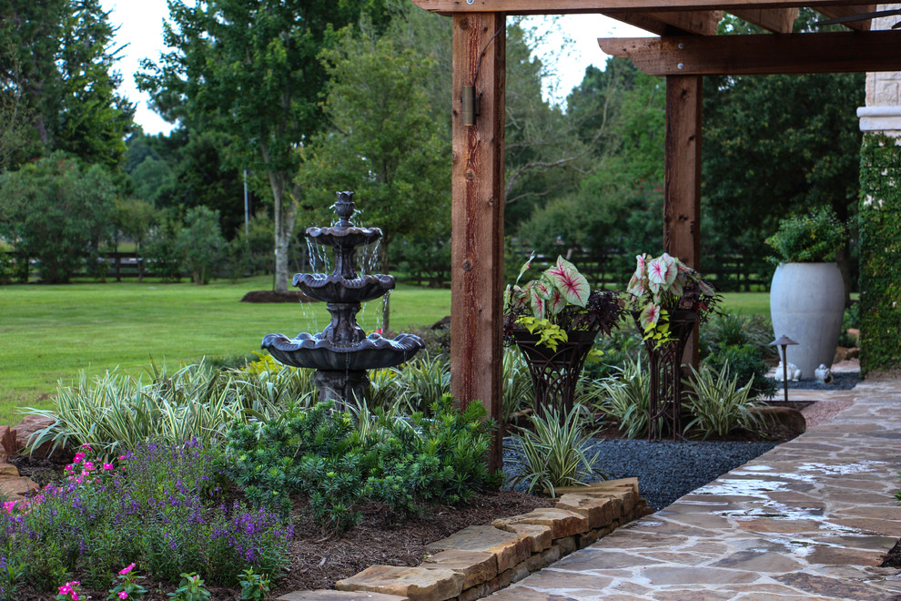 This is an example of a large front yard patio in Houston with a water feature, natural stone pavers and a pergola.