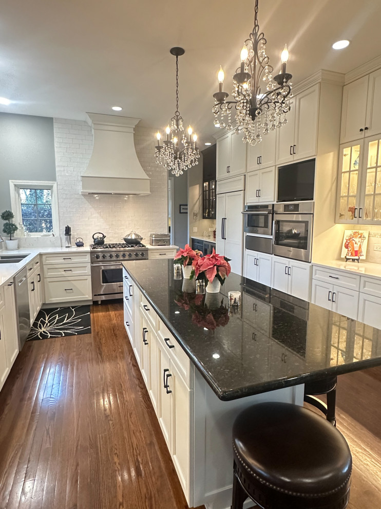 Example of a large classic u-shaped medium tone wood floor and brown floor enclosed kitchen design in Chicago with an undermount sink, recessed-panel cabinets, white cabinets, white backsplash, stainless steel appliances and an island