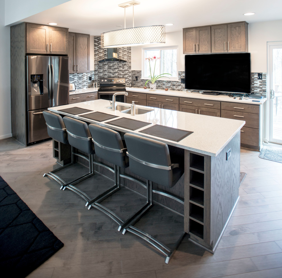 Inspiration for an expansive modern u-shaped eat-in kitchen in Baltimore with a drop-in sink, shaker cabinets, grey cabinets, quartz benchtops, grey splashback, mosaic tile splashback, black appliances, light hardwood floors and with island.