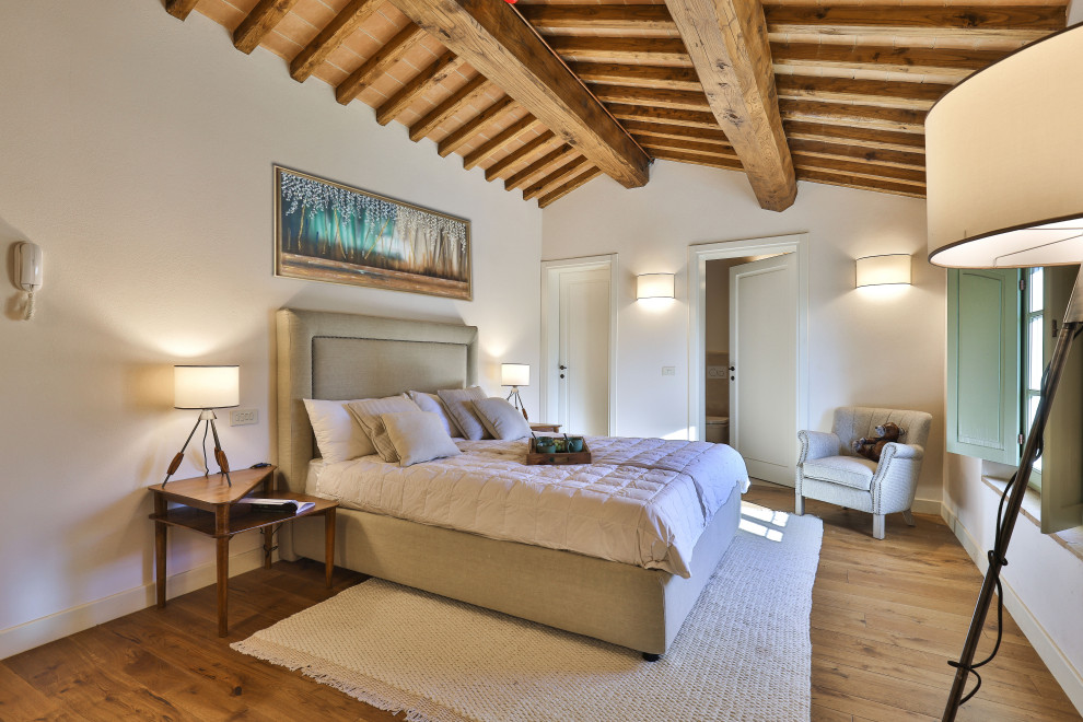 Immagine di una grande camera degli ospiti country con pareti beige, pavimento in legno verniciato, pavimento marrone e travi a vista
