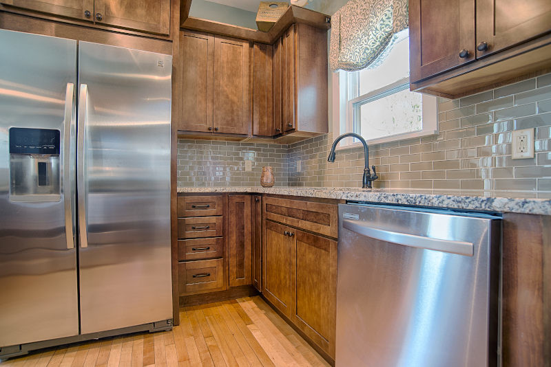 Mid-sized arts and crafts u-shaped separate kitchen in Cleveland with an undermount sink, glass-front cabinets, medium wood cabinets, granite benchtops, beige splashback, subway tile splashback, stainless steel appliances and light hardwood floors.