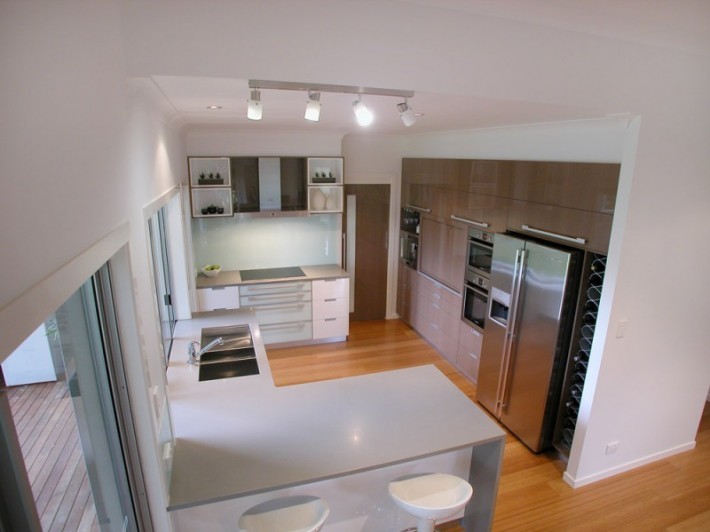 This is an example of a contemporary kitchen in Sydney with a double-bowl sink, flat-panel cabinets, white splashback, glass sheet splashback, stainless steel appliances and light hardwood floors.