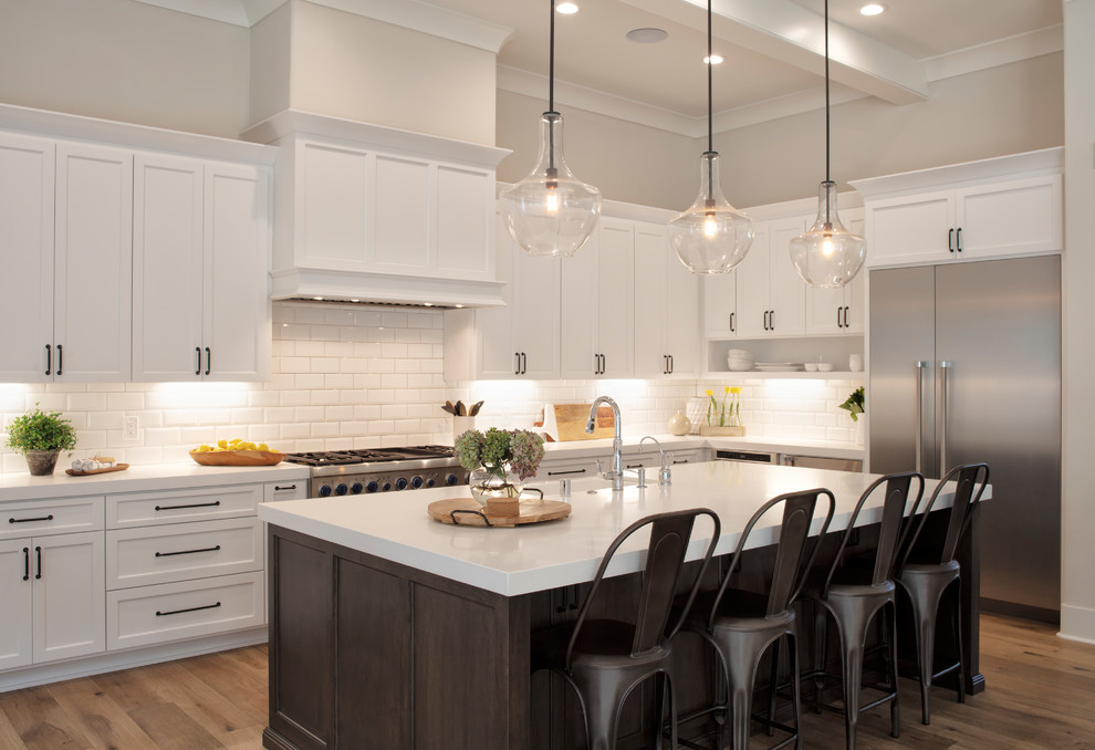Example of a mid-sized farmhouse l-shaped medium tone wood floor and brown floor kitchen design in San Francisco with a farmhouse sink, white cabinets, quartz countertops, white backsplash, subway tile backsplash, stainless steel appliances, an island, white countertops and shaker cabinets