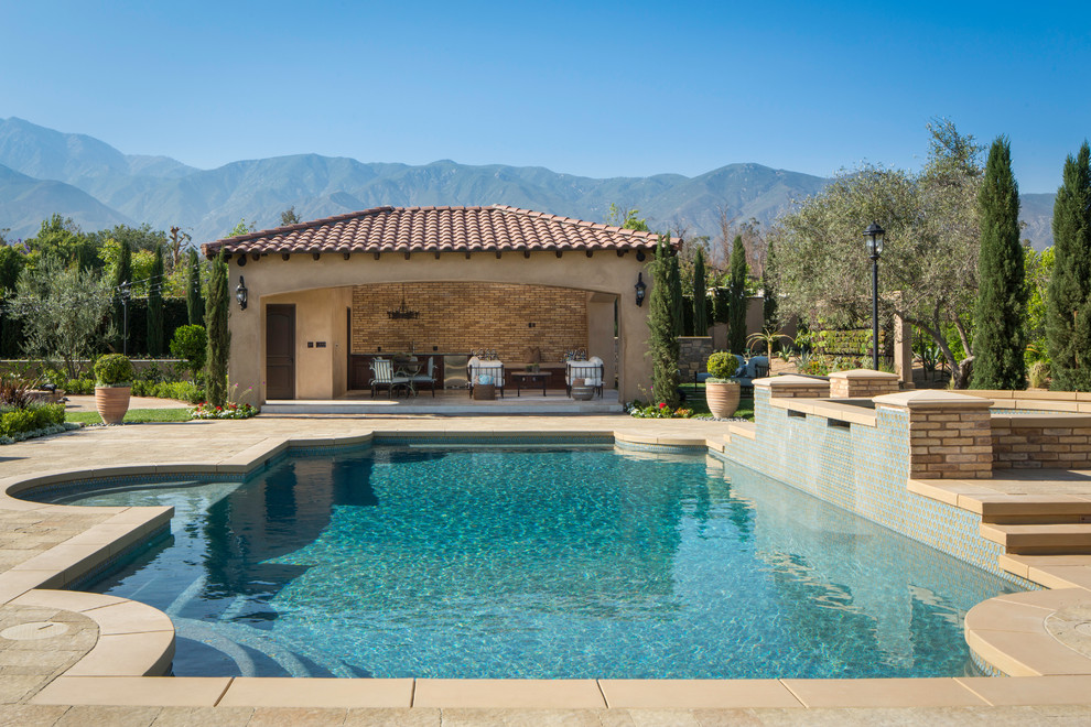 This is an example of an expansive mediterranean backyard custom-shaped pool in Los Angeles with natural stone pavers and a hot tub.