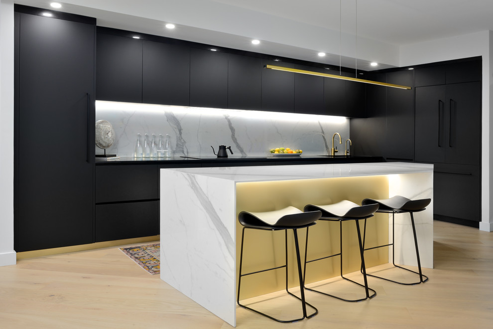 Design ideas for a contemporary kitchen in Toronto with flat-panel cabinets, black cabinets, white splashback, stone slab splashback, light hardwood floors, with island, beige floor and black benchtop.