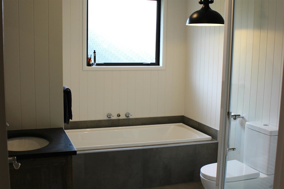 Photo of a small traditional bathroom in Auckland with a drop-in tub, a corner shower, white walls, ceramic floors, an undermount sink, a hinged shower door and black benchtops.