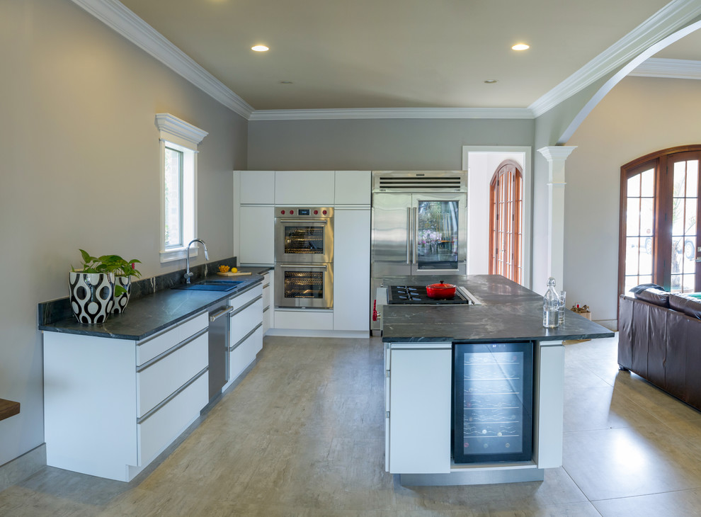 Contemporary l-shaped eat-in kitchen in New Orleans with an undermount sink, flat-panel cabinets, white cabinets, soapstone benchtops, grey splashback, stone slab splashback, stainless steel appliances, porcelain floors, with island, grey floor and grey benchtop.