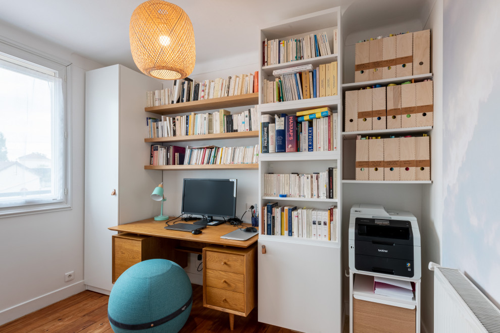 Mittelgroßes Modernes Arbeitszimmer ohne Kamin mit Arbeitsplatz, weißer Wandfarbe, braunem Holzboden, freistehendem Schreibtisch, braunem Boden und Tapetenwänden in Paris