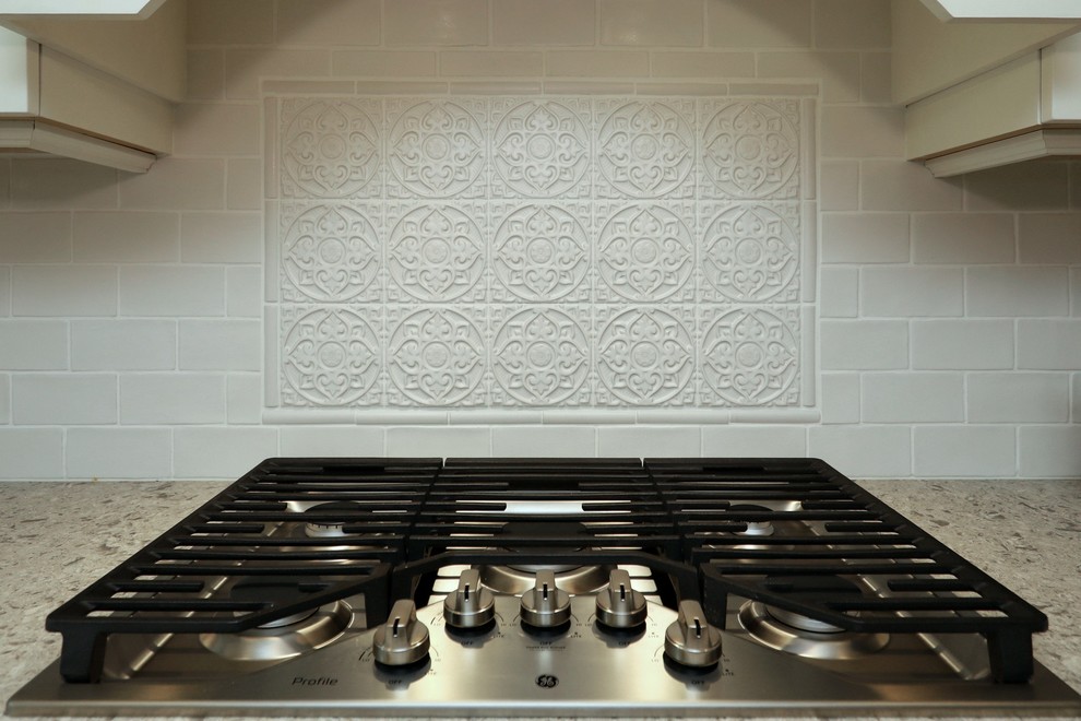 Example of a transitional vinyl floor and brown floor kitchen design with an undermount sink, white cabinets, quartz countertops, white backsplash, subway tile backsplash, stainless steel appliances, an island and beige countertops