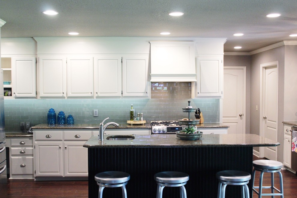 Example of a mid-sized transitional l-shaped dark wood floor and brown floor enclosed kitchen design with an undermount sink, raised-panel cabinets, white cabinets, granite countertops, gray backsplash, glass tile backsplash, stainless steel appliances and an island