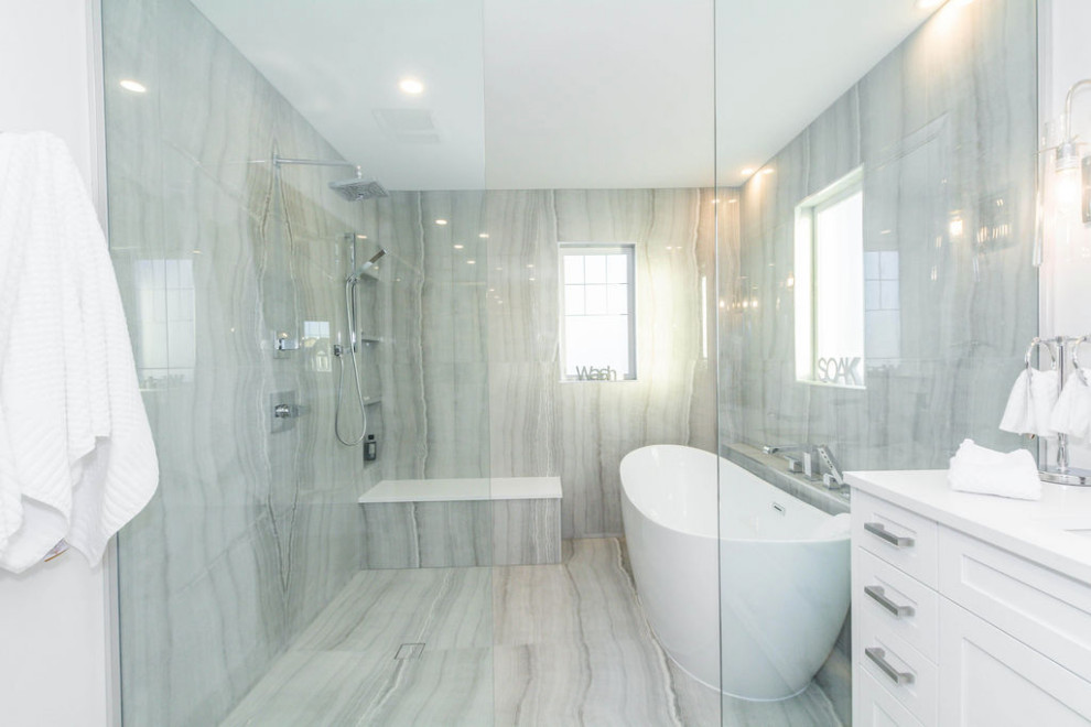 This is an example of a mid-sized contemporary master wet room bathroom in Edmonton with shaker cabinets, white cabinets, a freestanding tub, a two-piece toilet, gray tile, ceramic tile, grey walls, porcelain floors, an undermount sink, engineered quartz benchtops, grey floor, an open shower, white benchtops, a shower seat, a double vanity and a built-in vanity.
