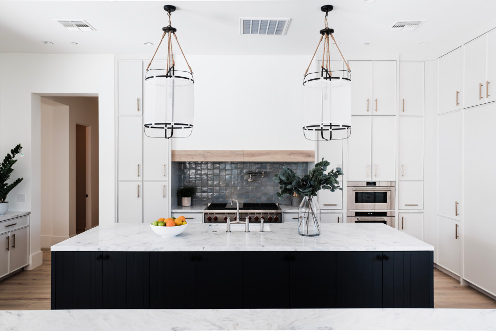 Transitional u-shaped medium tone wood floor and brown floor open concept kitchen photo in Phoenix with an undermount sink, recessed-panel cabinets, white cabinets, gray backsplash, paneled appliances, an island and gray countertops
