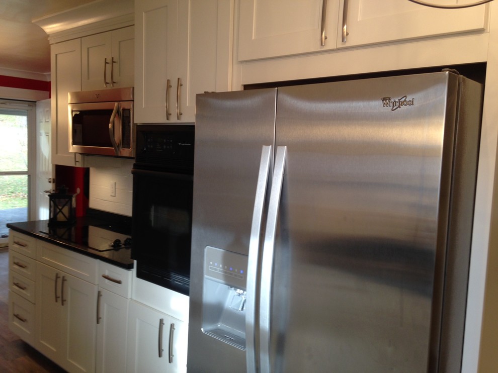 Mid-sized arts and crafts u-shaped vinyl floor home design photo with a double-bowl sink, shaker cabinets, white cabinets, quartz countertops, white backsplash, porcelain backsplash, stainless steel appliances and no island